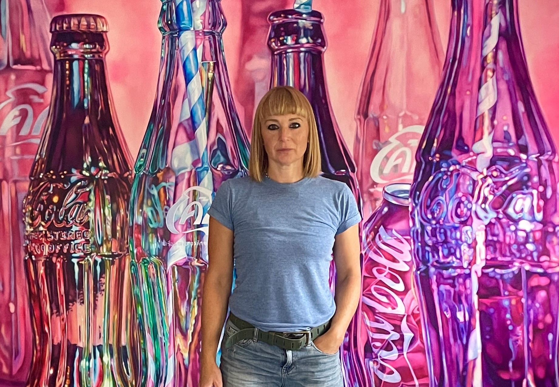 Artist Kate Brinkworth stands in her studio in front of a painting of giant pop bottles, part of the women in art exhibition, HER, at Maddox Gallery.